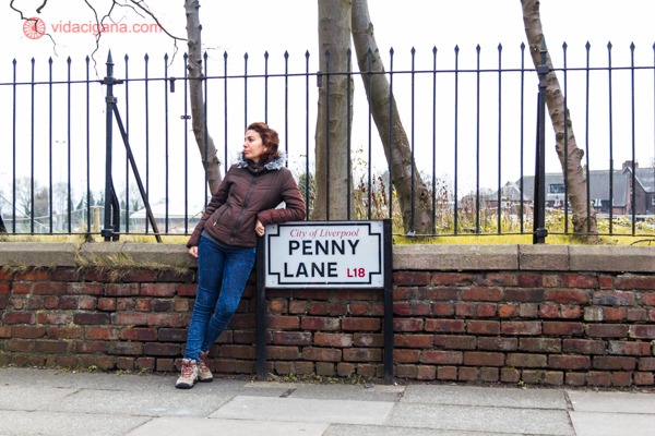 Onde ficar em Liverpool: uma mulher encostada na placa da rua Penny Lane, em Liverpool