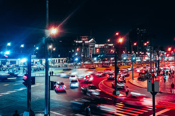 O trânsito no centro de Lima, com vários carros à noite e seus prédios ao fundo