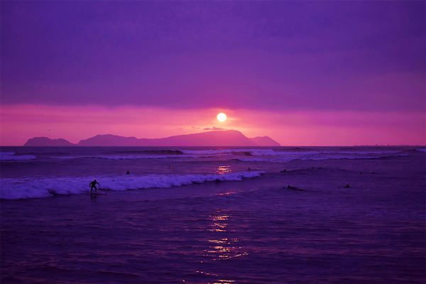 Onde ficar em Lima: o pôr do sol visto de uma praia em Miraflores, com alguns surfistas ao mar