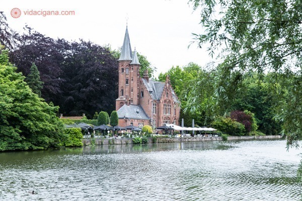 Um prédio de tijolos ocre na beira do rio que contorna a cidade de Bruges