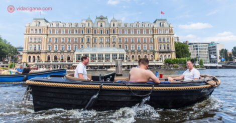O que fazer em Amsterdam: três homens andando de barco na frente de um grande hotel em Amsterdam