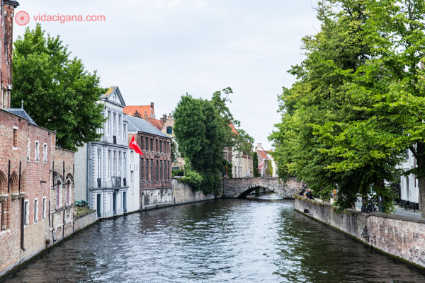 Um dos canais em Bruges com várias casas encostadas no rio e árvores verdes