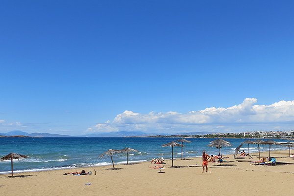 Uma das praias da Riviera ateniense, com águas claras, areia amarela e guardas sol