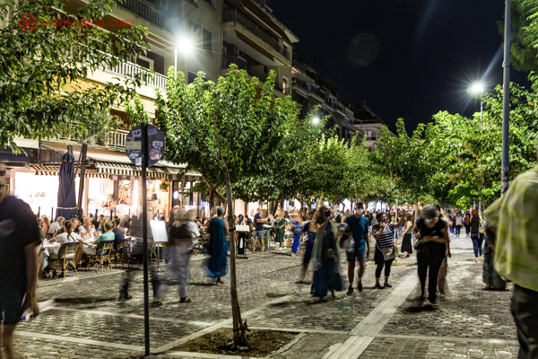 A Rua Adrianou à noite, repleta de pessoas na rua e restaurantes lotados.