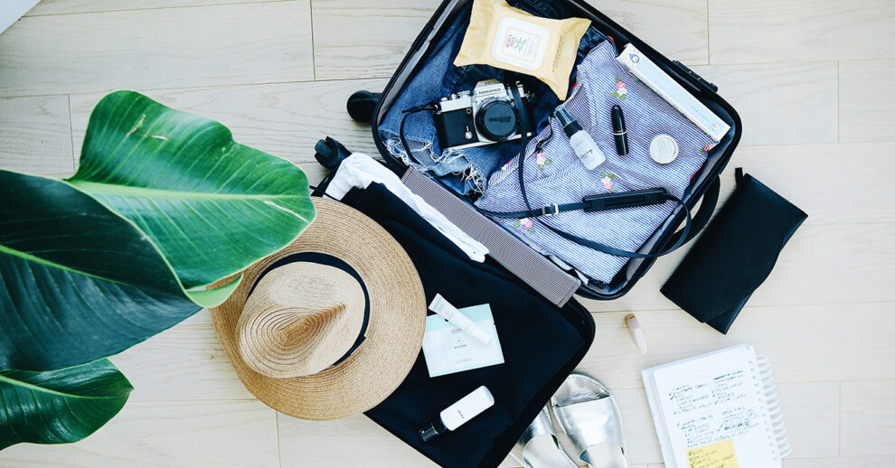 Coberturas de seguro viagem: uma mala aberta com câmera, chapéu, roupas e caderno