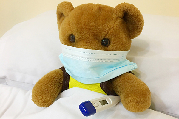 Regresso Sanitário: um ursinho de pelúcia com máscara e termômetro deitado numa cama