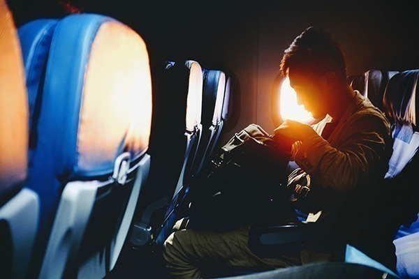 Um homem olhando dentro da mochila dentro de um avião durante o pôr do sol