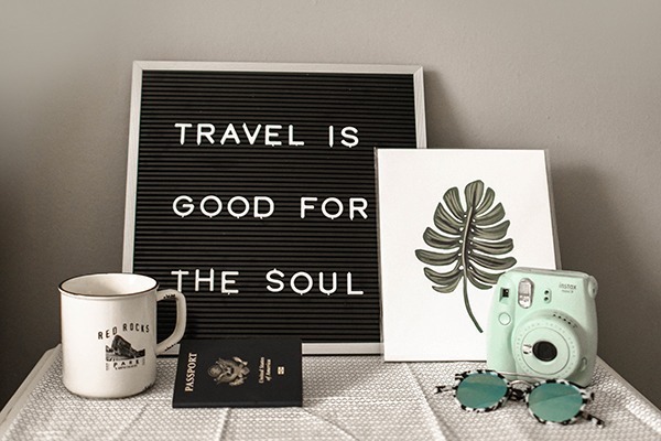 Foto de uma placa preta com palavras em branco onde se lê Travel is good for the soul.