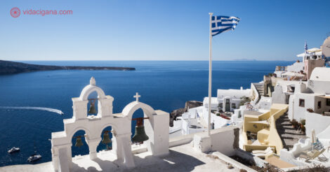 O que fazer em Santorini: os sinos de uma igreja com o mar ao fundo e a bandeira da Grécia tremulando