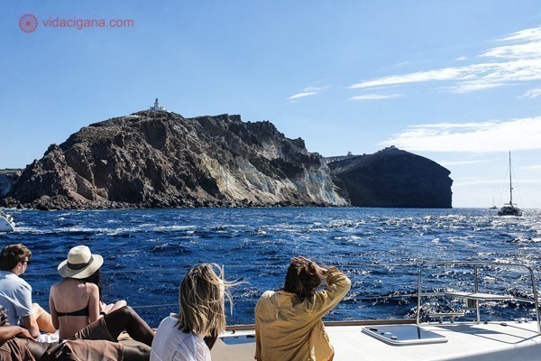 Pessoas em um iate olhando para o farol de Santorini num dia ensolarado