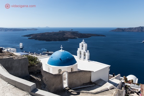 A igreja Three Bells of Fira, branca com a cúpula azul, e o mar ao fundo com as outras ilhas