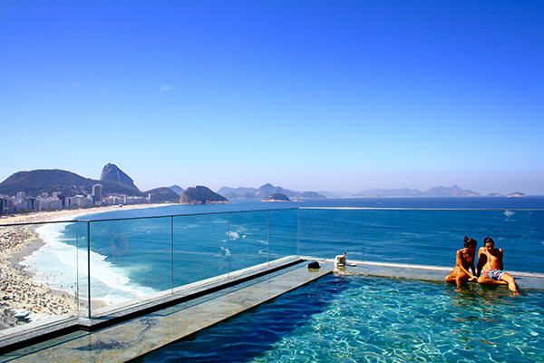 Um casal sentado na piscina de borda infinita de frente para a Praia de Copacabana