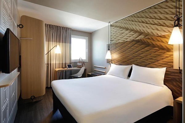 Um quarto de hotel com cama branca, parede com papel de parede bege