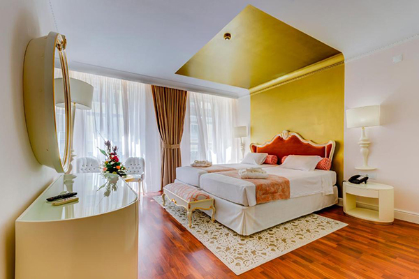 Um quarto com uma enorme cama com cabeceira vermelha e a parede dourada, com enormes janelas