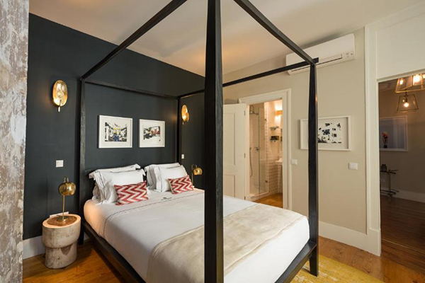 Um quarto com uma parede off white e outra preta, com uma cama grande e ar condicionado