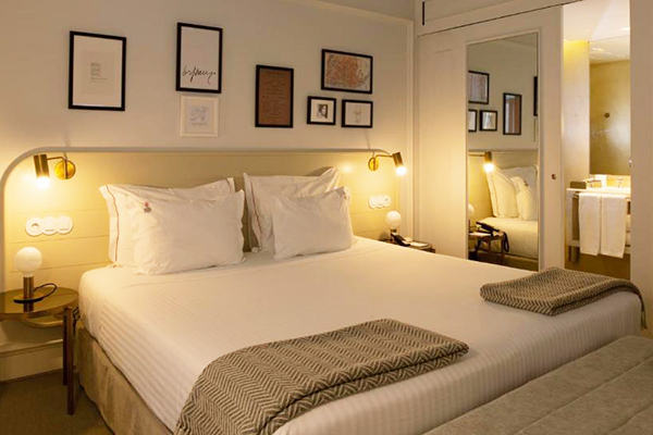 Um confortável quarto com cama branca, cabeceira cinza e luminárias amarelas