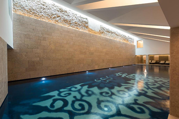 Uma piscina indoor envolta em paredes bege e o fundo da piscina possui desenhos azuis lindos