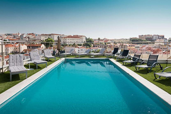 Uma piscina enorme com gramado ao redor e espreguiçadeiras, e vista de toda Lisboa
