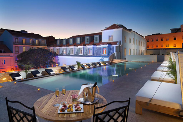 Hotéis com piscina em Lisboa: uma piscina de hotel durante a noite, com espreguiçadeiras brancas e vista para dentro do pátio do hotel
