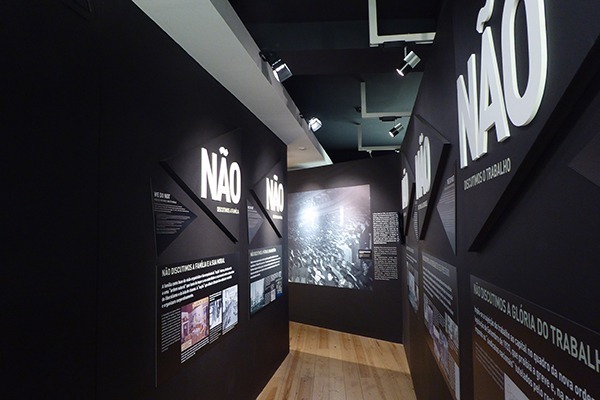 O interior do Museu do Aljube, com seu interior preto, e várias placas explicativas em branco e com fotos