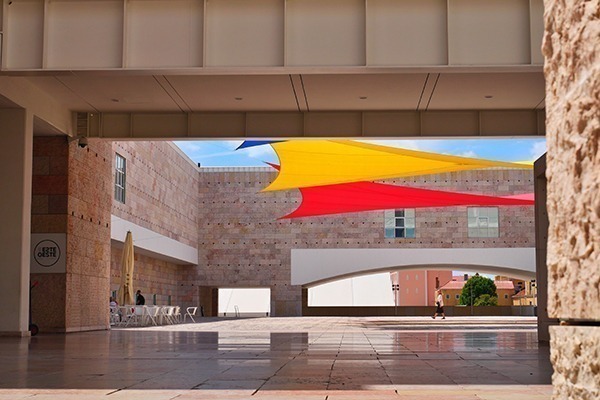 O pátio de dentro do Museu Coleção Berardo, com mesas e cadeiras, e bandeiras coloridas no vão aberto