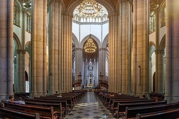 O interior da Catedral da Sé, toda branca, com a nave a igreja contendo vários candelabros