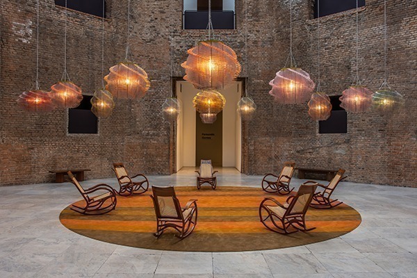 Um dos espaços da Pinacoteca de São Paulo, com várias cadeiras de balanço dispostas em círculos e luminárias pendendo do teto