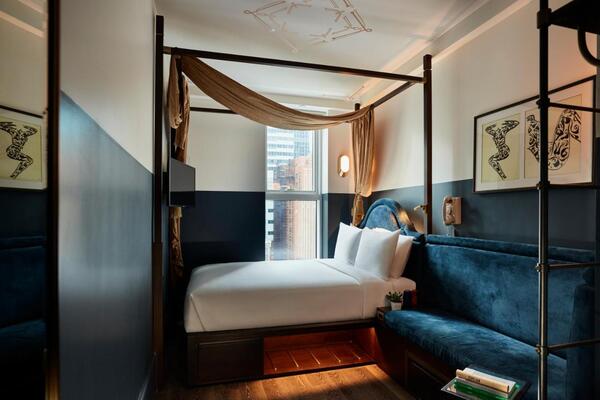 hotéis perto da times square, quarto com cama de casal e paredes pintadas na cor azul. Um sofá cama na mesma tonalidade e aspecto felpudo complementa a cena.