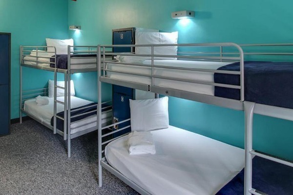 2 camas beliches com lençóis brancos e cobertores azul marinho, a parede é azul-esverdeada