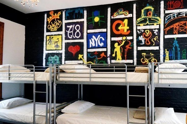 3 beliches de metal cinza com lençóis brancos e parede de trás grafitada com referências de Nova York