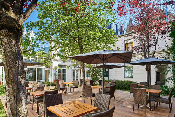 Hotéis baratos em Paris: o pátio de um hotel cheio de árvores e mesas com guarda sol