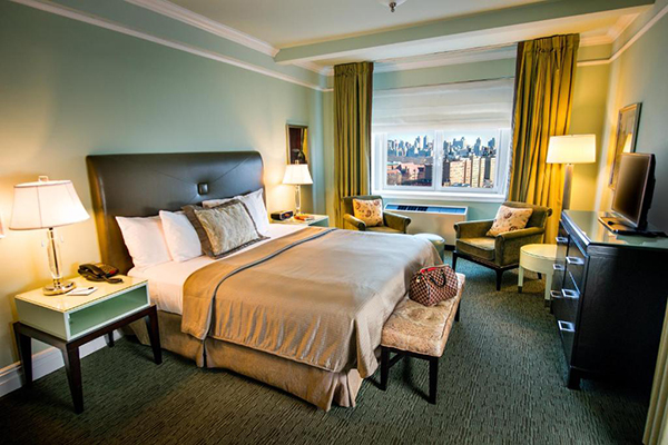 Quarto de hotel com cama com cabeceira marrom, janela com vista para a cidade de Nova York