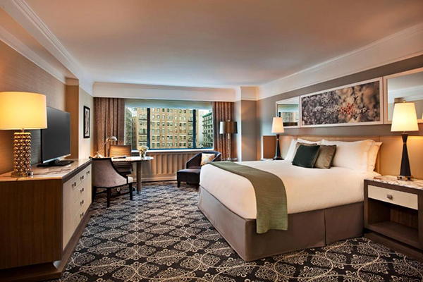 Quarto de hotel espaçoso com cama alta branca com detalhes verdes. Janela grande com vista para a cidade de Nova York