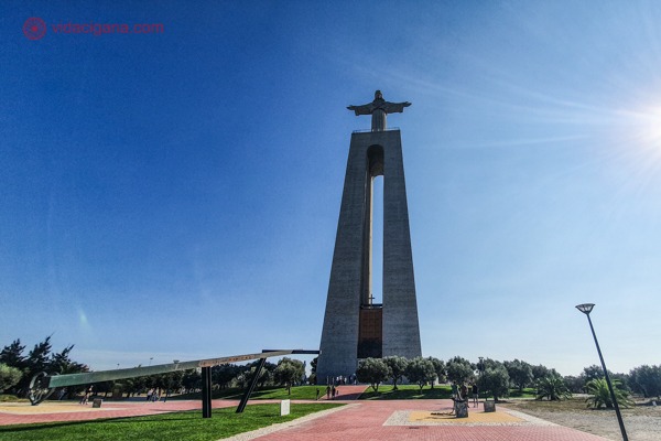 A estátua do Cristo Rei acima de uma torre oca com os braços abertos num dia de sol