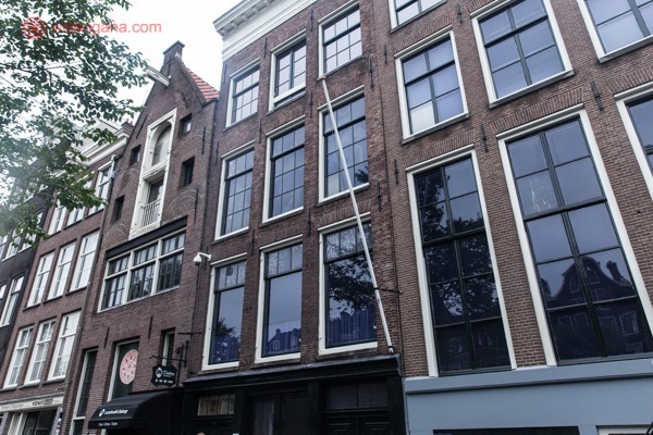 A Casa de Anne Frank do lado externo, um prédio de tijolos com de ocre com janelões de vidro