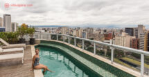 Onde ficar em São Paulo: Uma mulher ruiva sentada na beira da piscina, de onde dá pra ver toda a cidade de São Paulo