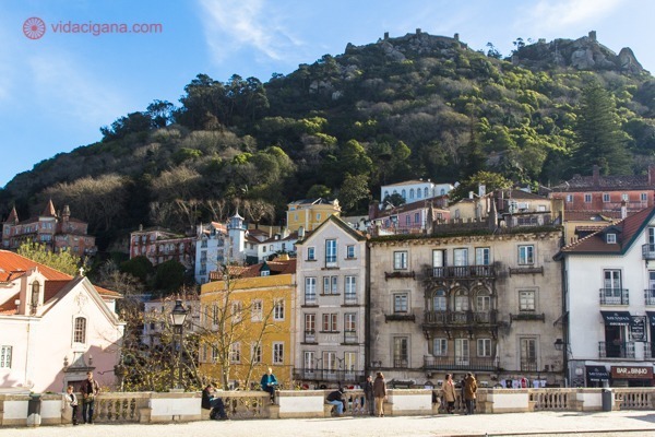 A Vila de Sintra cheia de prédios baixos e antigos, muito verde com as montanhas ao fundo e o Castelo dos Mouros no topo