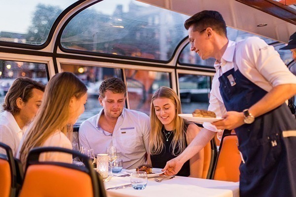 Um garçom servindo o jantar a 2 casais sentados dentro do barco