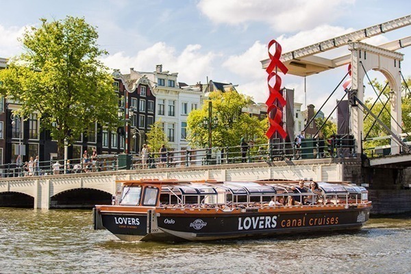 Um barco comprido laranja e cinza passando por uma das pontes levadiças de Amsterdam