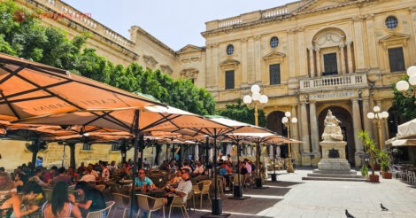 Onde ficar em Malta: várias pessoas sentadas em mesas embaixo de guarda-sóis na frente da Biblioteca de Valetta
