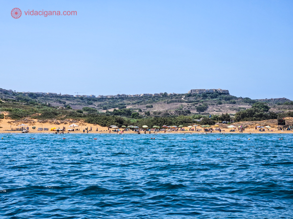Ramla Bay vista do mar, com suas areias douradas e colinas pedregosas ao fundo, com muito verde