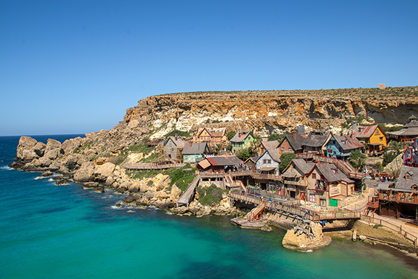 A Vila do Popeye vista de cima com suas casinhas de madeira na beira de um mar super azul.