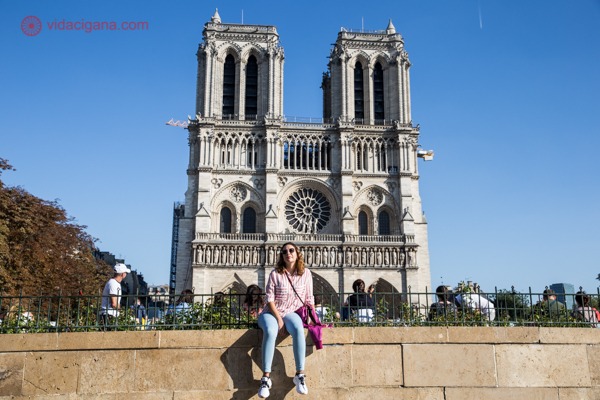 Eu sentada em uma mureta na frente da Catedral de Notre Dame