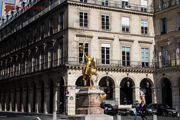 Uma rua do 1° arrondissement com a estátua de Joana d'Arc dourada em cima do cavalo