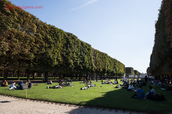 Várias pessoas deitadas no gramado do Jardim de Luxemburgo pegando um sol