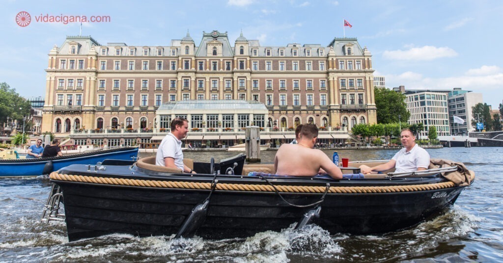 Clima em Amsterdam: homens andando de barco no rio Amstel em frente a um lindo hotel na beira do rio