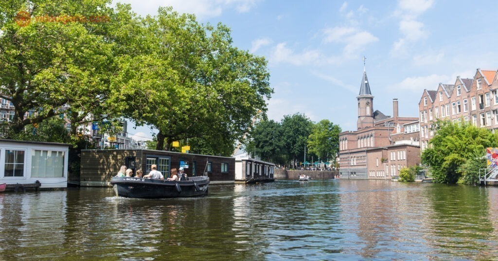 Pessoas sentadas num barco navegando por um dos canais de amsterdam, com uma igreja do lado direito