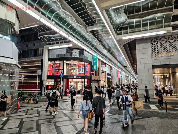 A movimentada Shinsaibashi-Suji Shopping Street em Osaka, Japão, uma rua coberta de pedestres com iluminação moderna e arquitetura contemporânea. Transeuntes passeiam entre as vitrines de lojas e sinalizações diversas, criando uma atmosfera urbana e comercial.




