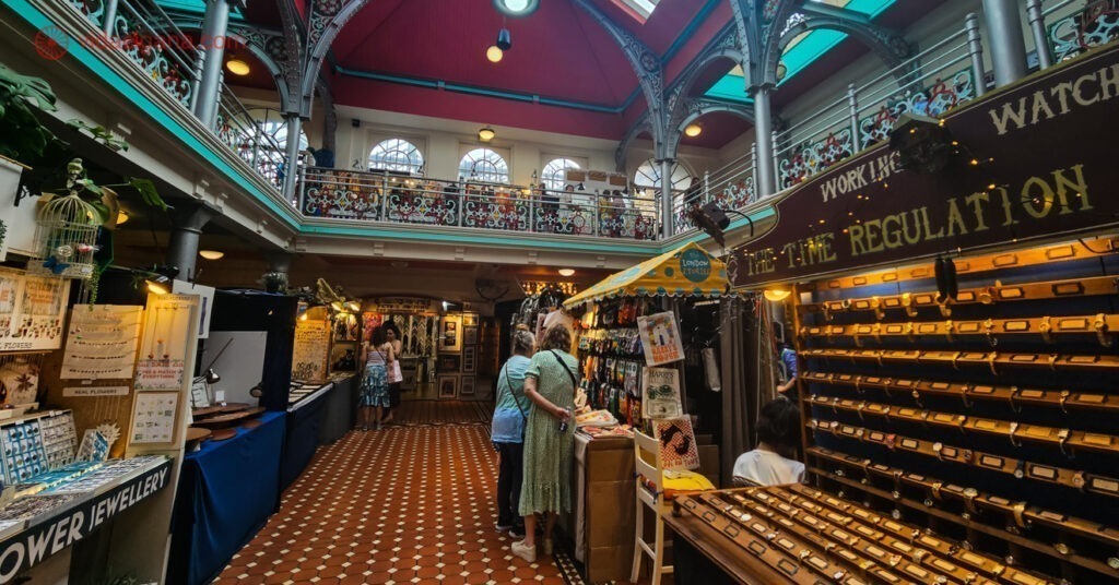 O interior do Camden Market é repleto de vendedores e barraquinhas. Na foto aparecem barracas de joias, relógios e artesanato, além de visitantes que apreciam o passeio.