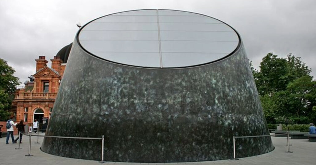 A imagem mostra a estrutura do Peter Harrison Planetarium. O prédio de formato circular interessante fica no Greenwich Parque, ao lado do Observatório Real, que podemos ver logo atrás.